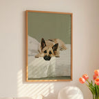 A contemporary oil-style art print of a German Shepherd lying on white bedding with alert ears, painted in warm honey tones against a soft sage green background.