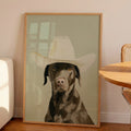 Minimalist oil painting print of a chocolate Labrador wearing an oversized cowboy hat, painted in warm brown tones against a soft sage green background