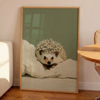 A contemporary oil-style art print of a hedgehog peeking out from white bedding, painted in warm cream and amber tones against a soft sage green background.