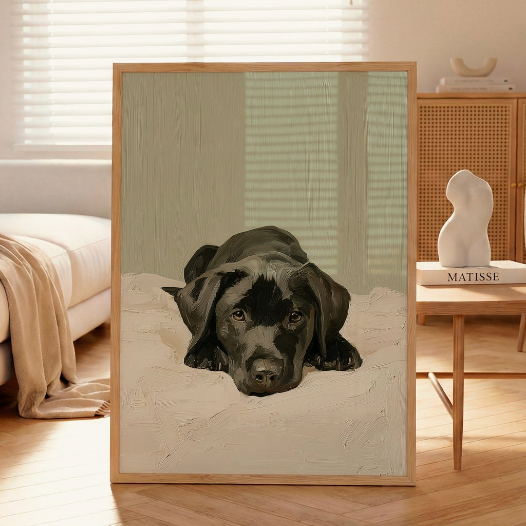 A contemporary oil-style art print of a black Labrador puppy lying on white bedding with a sleepy expression, painted in warm tones against a soft sage green background.
