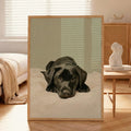 A contemporary oil-style art print of a black Labrador puppy lying on white bedding with a sleepy expression, painted in warm tones against a soft sage green background.
